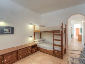 A bunk bed with a wooden ladder, a wooden dresser with drawers, and a framed picture on the wall.