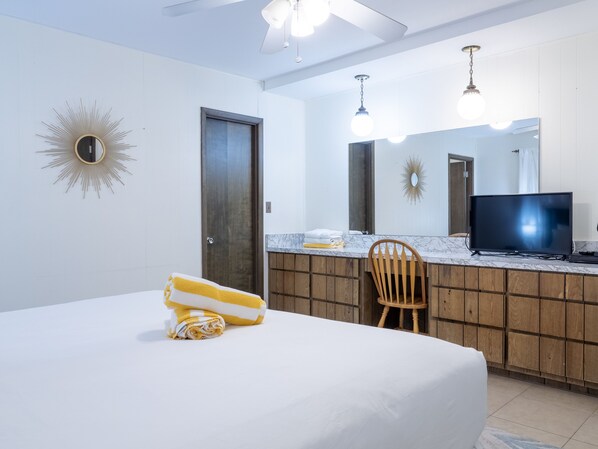 Ein Hotelzimmer mit einem Bett, einem Holzstuhl, einem Fernseher, einer Marmorplatte und einem großen Spiegel.
