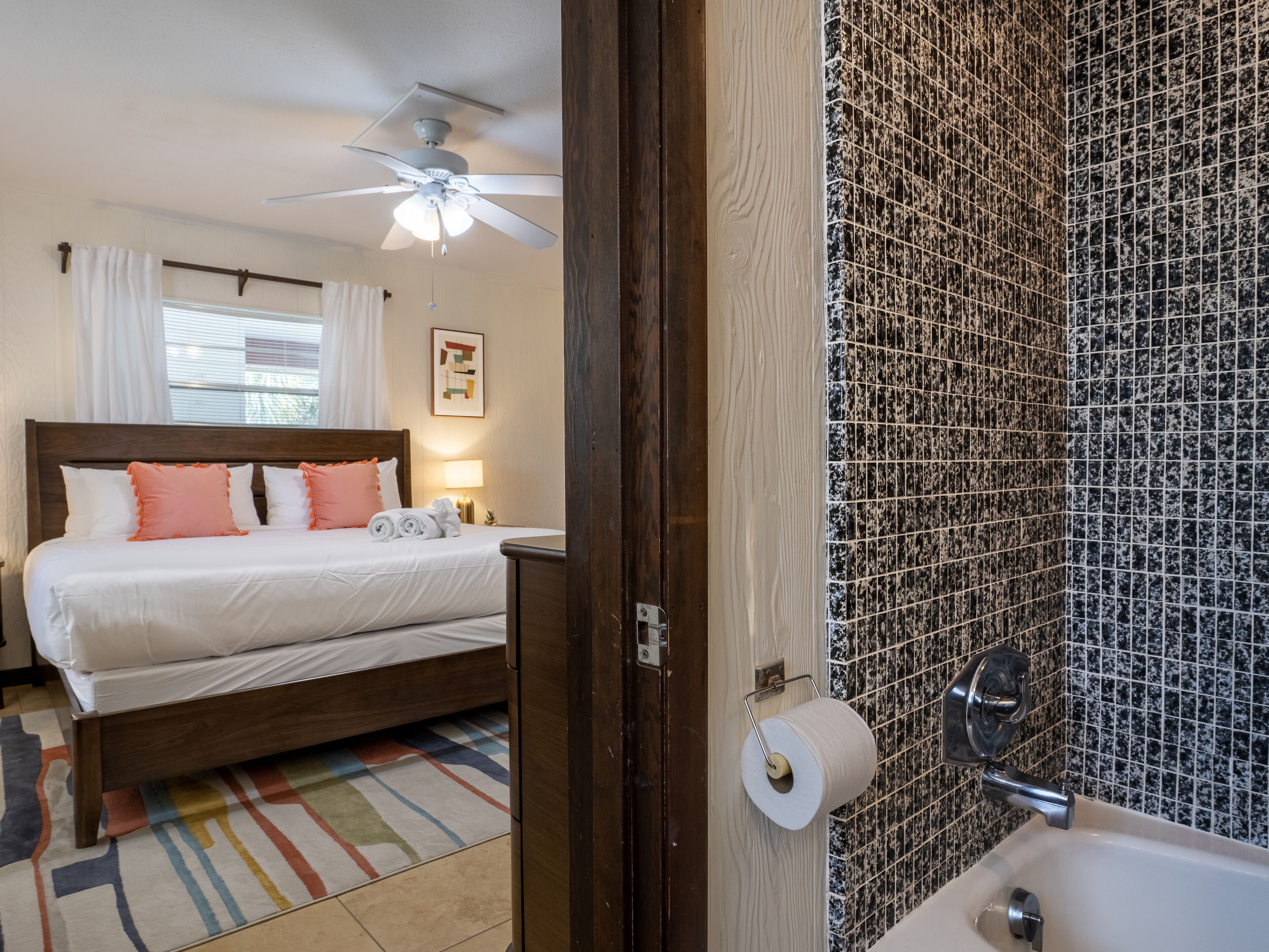 Une chambre d’hôtel avec un lit, un ventilateur de plafond et une salle de bain équipée d’un lavabo et d’un porte-rouleau de papier toilette.