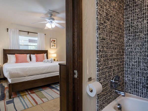 A hotel room with a bed, a ceiling fan, a bathroom with a sink and a toilet paper holder. - Bollinger B · Pet-Friendly · Half Block to Gulf (Holmes Beach)