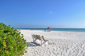 A sandy beach with a wooden bench and a red umbrella. - Bollinger B · Pet-Friendly · Half Block to Gulf (Holmes Beach)