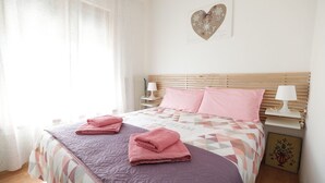 Un lit bien fait, avec des serviettes roses, une couvre-lit à motifs géométriques et une tête de lit en bois.