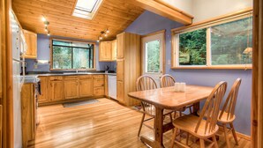 Une cuisine spacieuse avec des meubles en bois, une grande table à manger et une vue sur la forêt par les fenêtres.