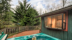 Un bain à remous sur une terrasse en bois, avec vue sur une forêt et un chalet.