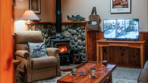 Un salon chaleureux avec une cheminée en pierre, une tête de cerf accrochée au mur, un téléviseur et une table basse en bois.