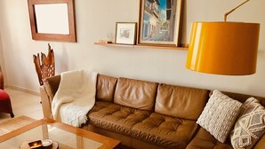 Uma sala de estar com um sofá de couro marrom, uma mesa de centro de vidro, uma mesinha de cabeceira de madeira e um abajur amarelo.