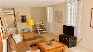 Uma sala de estar com sofá, mesa de centro, televisão, escada e um quadro na parede.