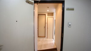 A narrow hallway with a wooden door at the end, a light switch on the wall, and a number sign indicating room 112. - Kanazawa-Hub (Kanazawa)