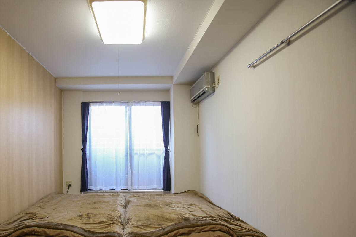 Quarto com cama, luminária no teto, ar condicionado e janela com cortinas.
