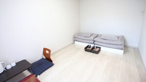 A small, bright room with a bed, a chair, a table, and a heater. - Kanazawa-Hub (Kanazawa)