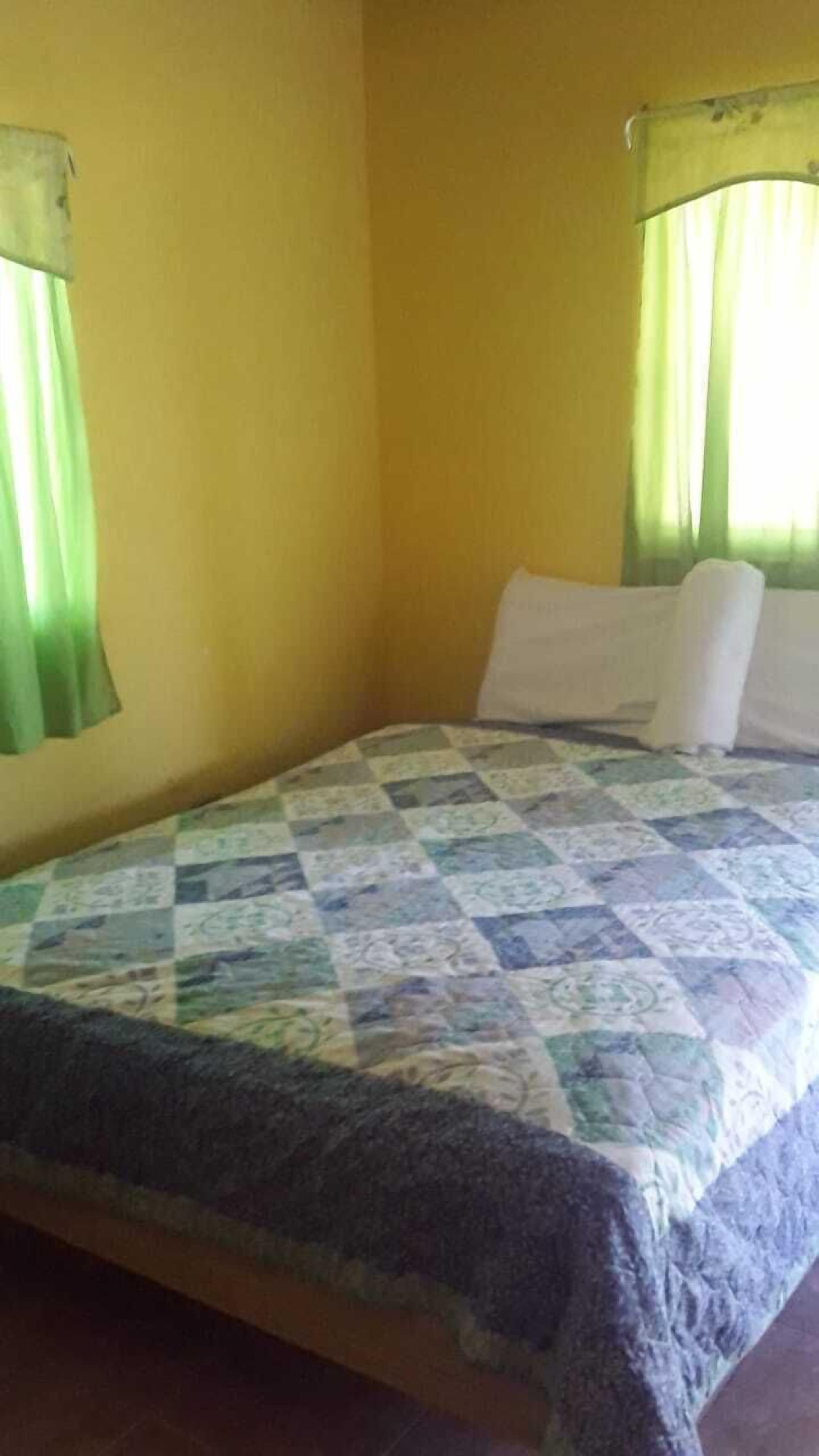 Una habitación con una cama, cortinas verdes y una pared amarilla.