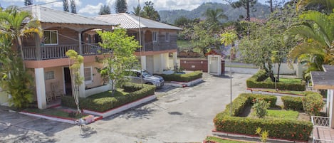 A two-story building with a balcony, surrounded by well-maintained gardens and a clear sky.