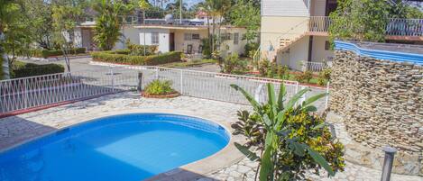Una piscina con bordo in pietra, circondata da un recinto bianco, adiacente a un edificio con un balcone.