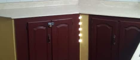 Una cocina en esquina con gabinetes de madera oscura, encimera blanca y piso de baldosas.