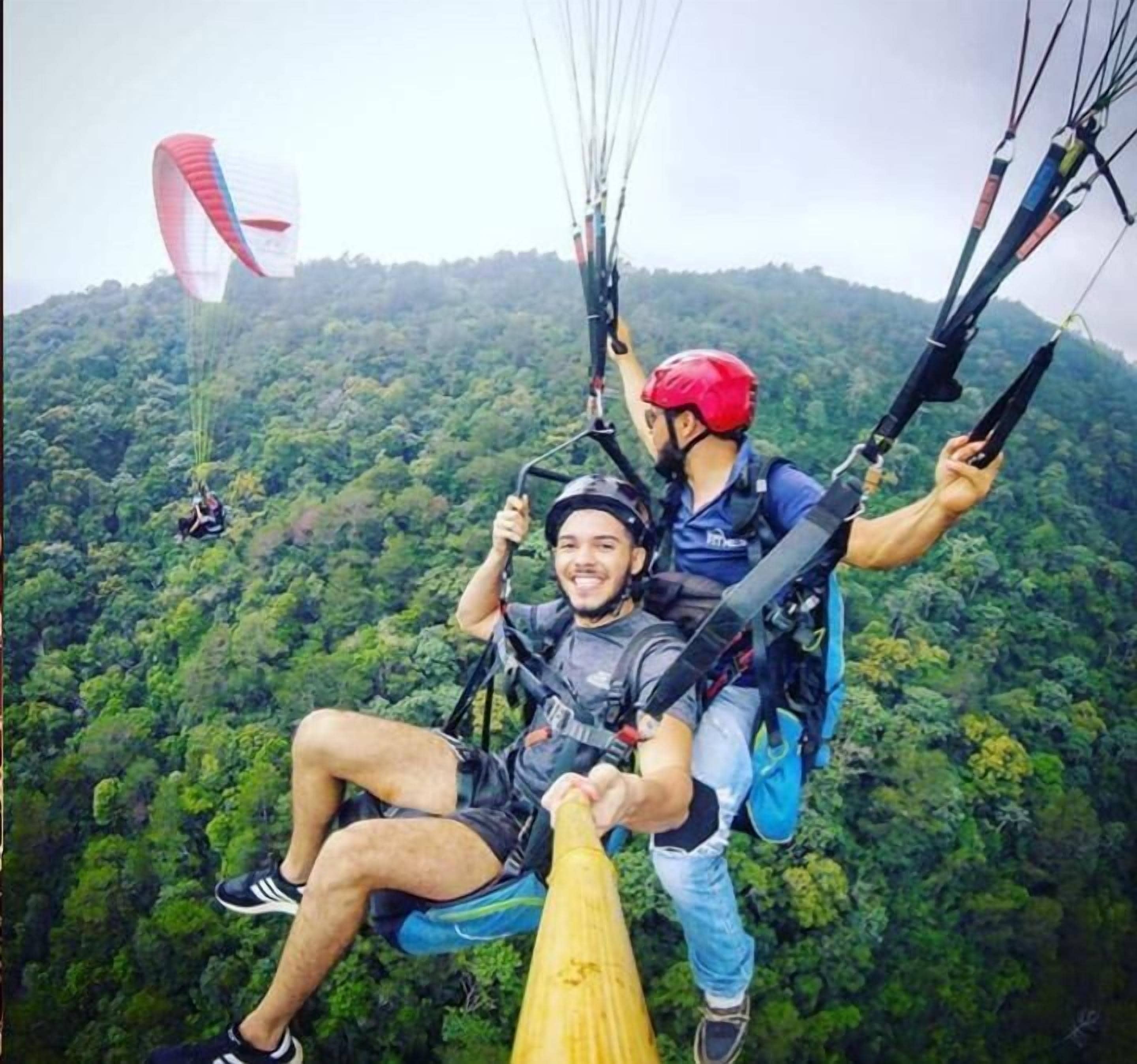 A person in a harness and helmet, secured with a parachute, being assisted by another person.