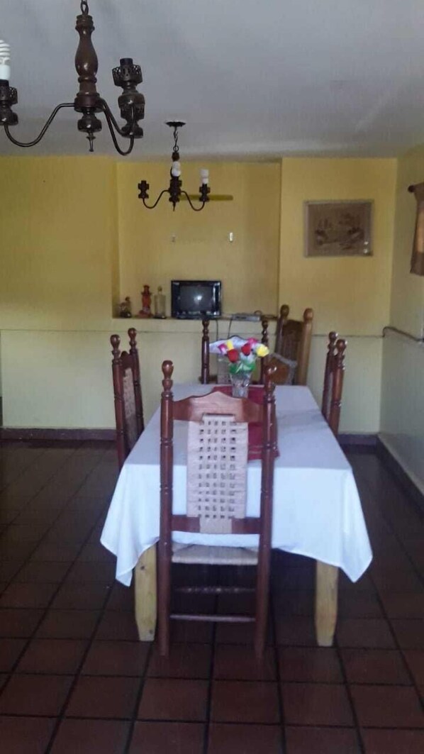 A dining area with a table set for four, a chandelier, and a television on the wall.