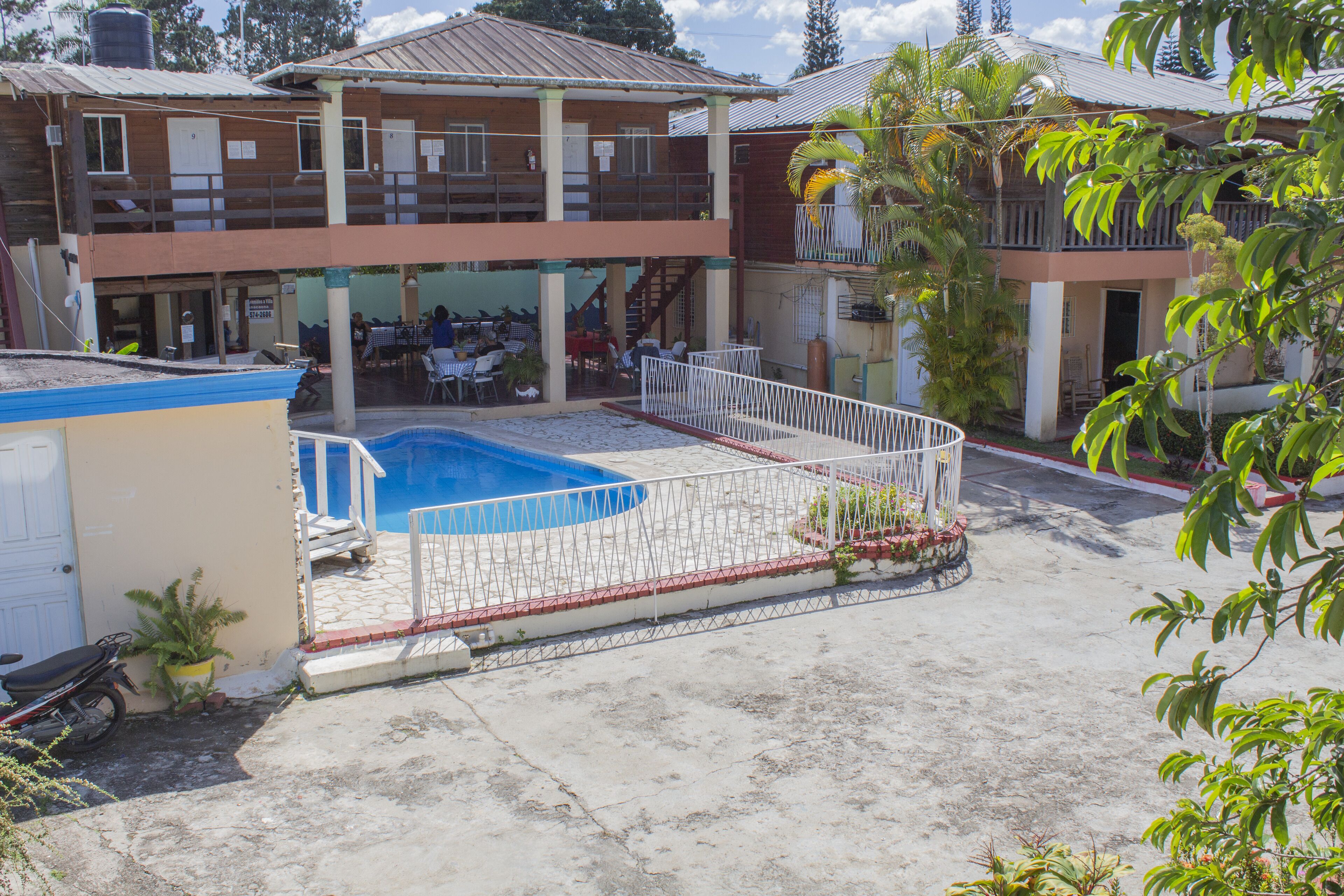 A two-story building with a swimming pool, outdoor seating, and a fenced area.