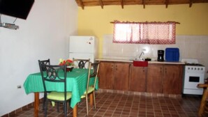 A compact kitchen with a dining table, chairs, a refrigerator, a sink, a coffee maker, and a stove. - Villas Anacaona (Jarabacoa)