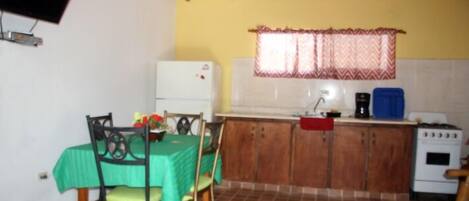 A compact kitchen with a dining table, chairs, a refrigerator, a sink, a coffee maker, and a stove.