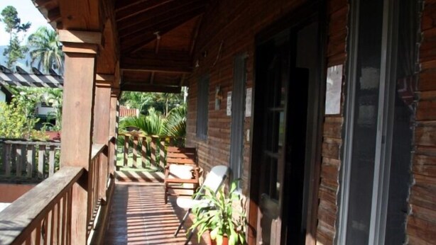 A covered wooden corridor with a tiled floor, potted plants, and a view of the surrounding greenery. - Villas Anacaona (Jarabacoa)