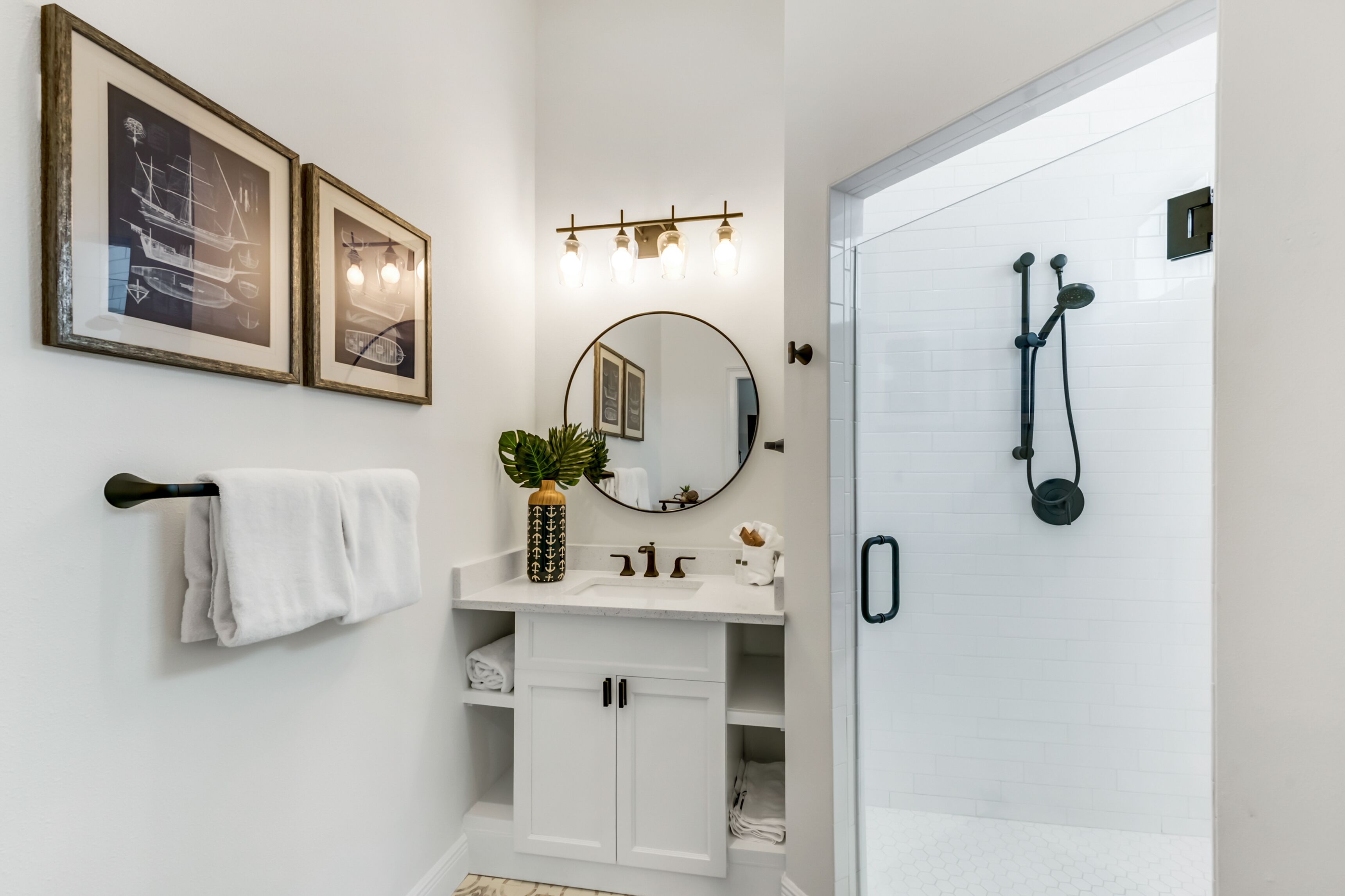 A bathroom with a white vanity, a round mirror, a towel rack, and a shower with a handheld showerhead.