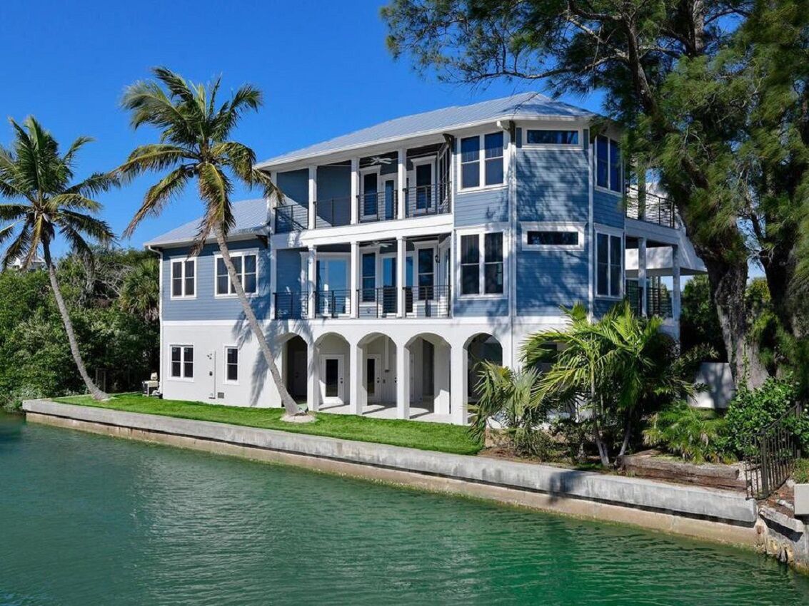 A large, multi-story house with a balcony, located near a body of water.