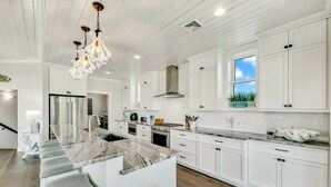 A modern kitchen with white cabinetry, a marble island, and a hanging light fixture.