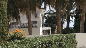 A well-maintained hedge, a tiled walkway, and a white building with a balcony. - Mediterranean dream (Oroklini)