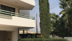A modern multi-story building with balconies, a tall cypress tree, and a palm tree. - Mediterranean dream (Oroklini)