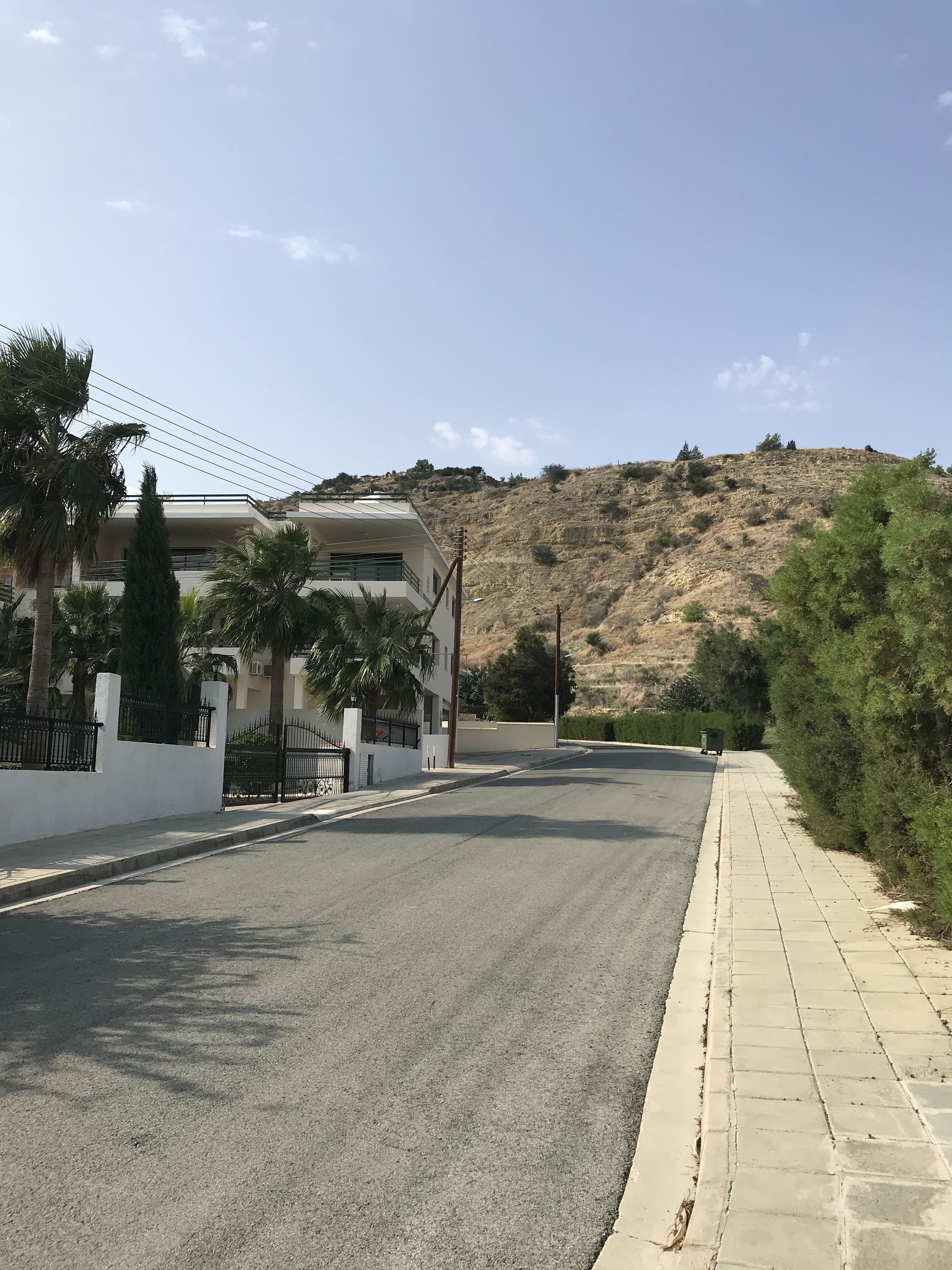 Una calle residencial tranquila con una casa moderna, cielo despejado y un paisaje montañoso al fondo.