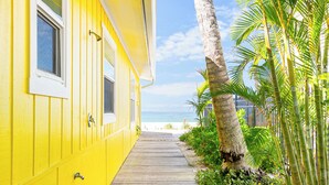 A yellow building with a wooden walkway leading to a beach. - Four Beach Lovers 4 · Full-Size Garden Unit · Solar · Gulf in 50 Steps (Holmes Beach)