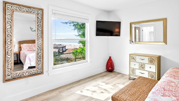 A bedroom with a large window, a bed, a dresser, and a TV on the wall.