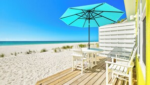 A beachside deck with a table and chairs, a blue umbrella, and a view of the ocean.