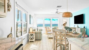 A spacious living room with a view of the ocean, a ceiling fan, and a large TV mounted on the wall.