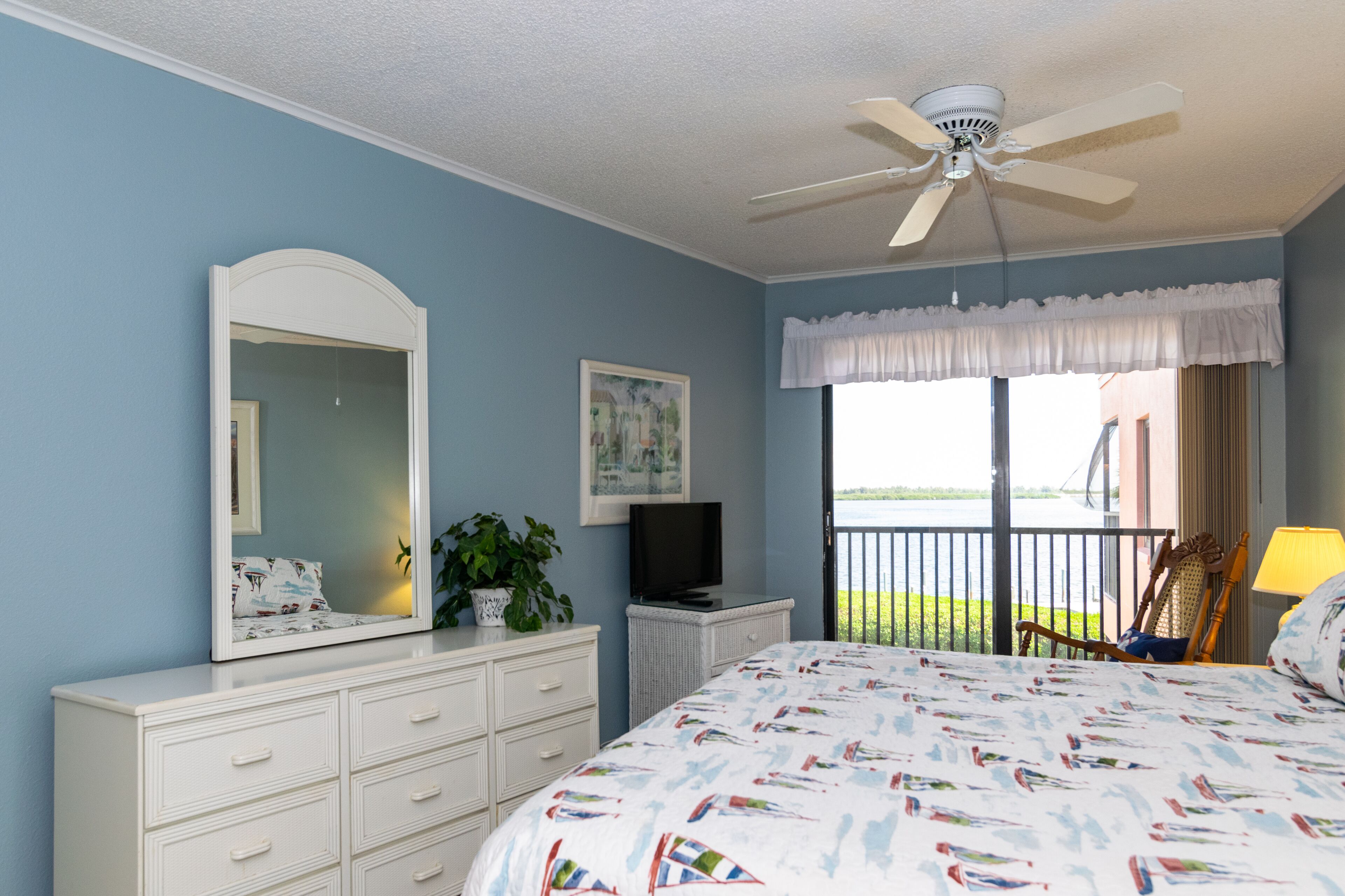 Une chambre à coucher comprenant un lit, une commode, un téléviseur et un ventilateur de plafond.