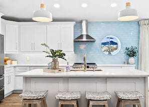 Cozinha moderna com armários brancos, uma ilha grande, banquetas, luminárias pendentes e painel de azulejos azul.