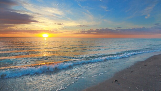 A beach with waves and a sunset.