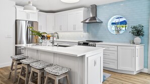 A modern kitchen with white cabinetry, a stainless steel refrigerator, a gas stove, and a large island with bar stools.