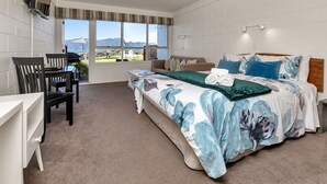 A bedroom with a large bed, a desk, and a chair. There are windows with a view of mountains.