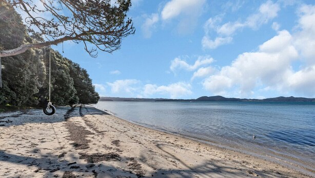 A beach with a tire swing, clear sky, and calm water.