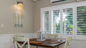 Un comedor con mesa de madera, sillas blancas, un farol y una ventana con persianas.