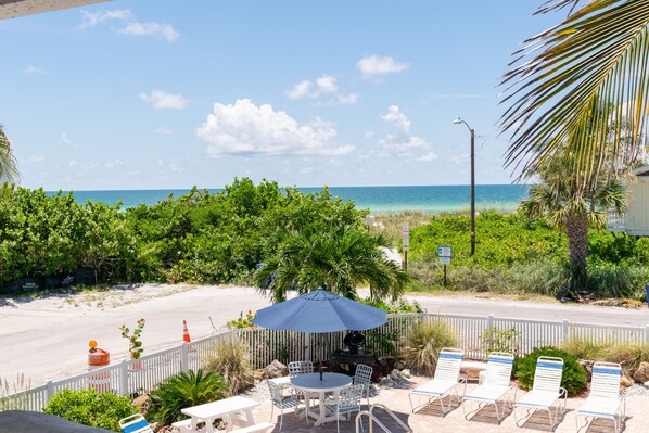 A beachside patio with a table and chairs, a blue umbrella, and a view of the ocean.