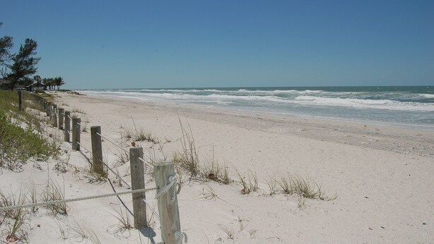 A sandy beach with a wooden fence and a clear blue sky.