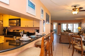 A kitchen with a central island, dining area with chairs, and a living room with a sofa.