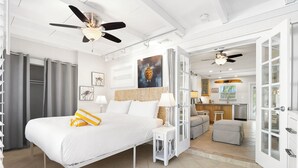 A modern hotel room with a large bed, a desk, and a kitchenette.