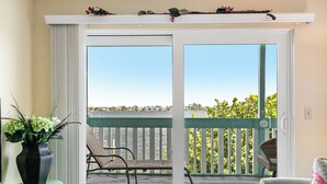 A balcony with a view of the water, a chair, and a small table with a vase of flowers. - Bay Watch 6A · Dock · Bay & Gulf Access (Bradenton Beach)
