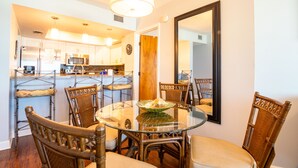 A dining area with a round glass table surrounded by six wooden chairs with cushioned seats. A large mirror hangs on the wall to the right.