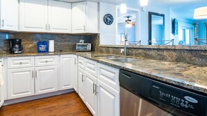 A modern kitchen with white cabinets, granite countertops, a dishwasher, a coffee maker, and a clock on the wall.