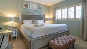 A bedroom with a large bed, bedside tables, a bench, and a window with curtains.