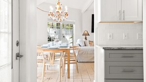 A modern kitchen with white cabinets, a dining area with a wooden table and chairs, and a chandelier.
